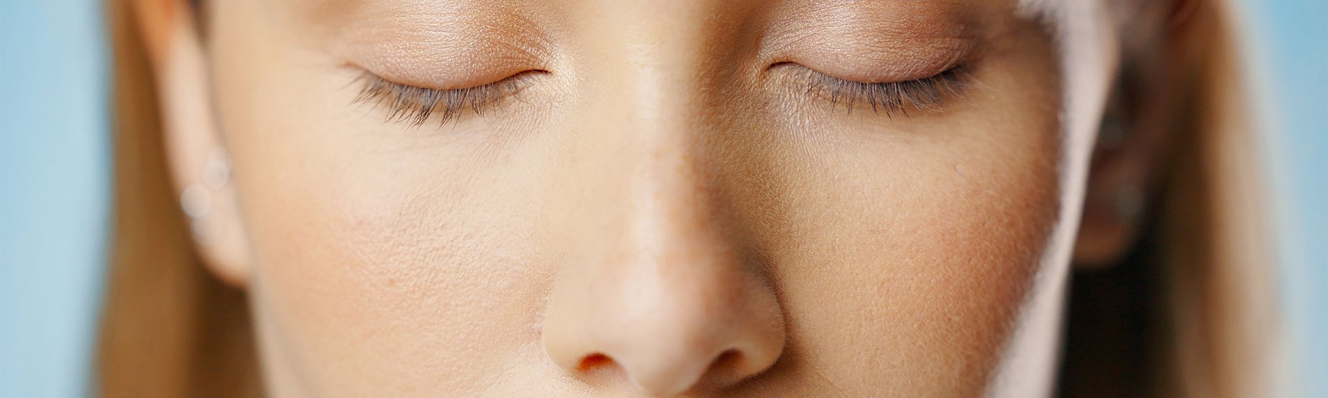 Close-up em rosto de mulher jovem e ruiva com olhos fechados e utilizando protetor solar com cor